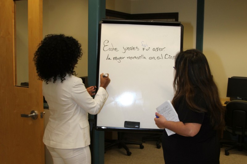 Two people writing in spanish on a whiteboard